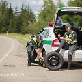 Akcijos &bdquo;Atsikratyk stereotipų&ldquo; fotosesijos kadras: kol kolega keičia tarnybinio automobilio ratą, jo porininkė lakuojasi nagus