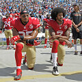 Ericas Reidas ir Colinas Kaepernickas neatsistojo per himną