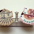 10 eurų ir 10 JAV dolerių banknotai ant svarstyklių 