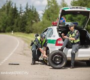 Akcijos &bdquo;Atsikratyk stereotipų&ldquo; fotosesijos kadras: kol kolega keičia tarnybinio automobilio ratą, jo porininkė lakuojasi nagus