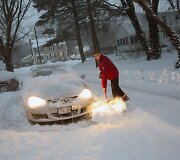 Vyras valo sniegą aplink savo automobilį.
