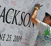 Žmonės pasira&scaron;inėja ant Michaelo Jacksono plakato.