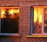 Liepsnos atspindžiai gretimų namų languose.