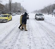 Žmonės eina per apsnigtą gatvę.