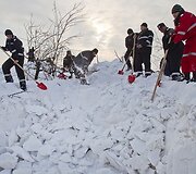 Gelbėtojai atkasinėja kelią į apsnigtą namą.