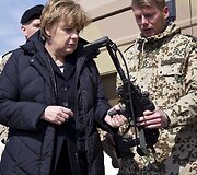Vokietijos kanclerė Angela Merkel laiko kulkosvaidį.