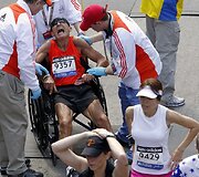 Medikai į vežimėlį sodina sunegalavusį Bostono maratono dalyvį.