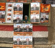 Moteris žiūri pro langą apkabinėta kandidato į prezidentus Abdel Moneimo Abol Fotouho plakatais.