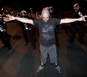 Prie&scaron; policininkus i&scaron;keltomis rankomis stovi protestuotojas