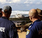 Australijos reindžeriai ir policininkai stovi netoli negyvo banginio.