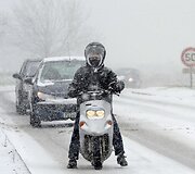 Ant apsnigto kelio stovi vyras su motoroleriu.