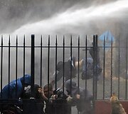 Nuo tvoros krenta protestuotojas, į kurį pataikė vandens patrankos srovė.