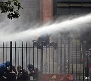 Nuo tvoros krenta protestuotojas, į kurį pataikė vandens patrankos srovė.
