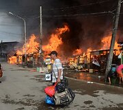 Vyras su savo daiktais eina netoli degančių namų