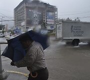Vyras po skėčiu slepiasi nuo vėjo ir lietaus