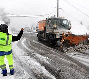 Darbuotojas laiko pakėlęs elektros laidus, kol pravažiuos kelią valanti ma&scaron;ina.