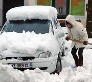 Moteris kasa sniegą &scaron;alia savo automobilio. 