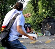 Studentas ruo&scaron;iasi mesti akmenis į riau&scaron;ių policijos automobilius.