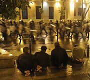 Prie gatvės sėdi sulaikyti protestuotojai.