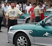 Taksi vairuotojas žiovauja &scaron;alia savo automobilio.
