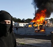 Vaikinas stovi netoli degančio namelio ant ratų