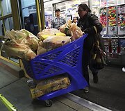 Moteris stumia prekių prikrautą vežimėlį.