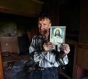 Vietos gyventojas laiko Kristaus paveikslą apgriautuose namuose