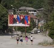 Pietų Osetijos gyventojai eina pro reklaminį plakatą, kuriame regiono prezidentas susitinka su Putinu