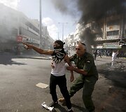 Palestiniečių pareigūnas bando sustabdyti akmenis mėtantį paauglį