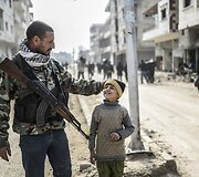 Sausio 26 diena. Kurdų kovotojas su sūnumi Kobanės miesto gatvėje 