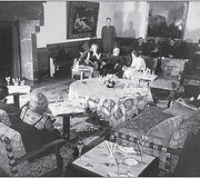 Eva Braun ir Hitleris ant sofos Berghofe, už jų stovi juos saugantis pareigūnas 