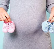 Nėščia moteris, rankose laikanti skirtingų spalvų vaikiškus batukus