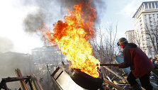 An anti-government protester moves a burning tyre at a barricade in Kiev February 21, 2014. Violence flared again in Kiev on Friday as Ukraine's opposition politicians pondered a draft deal with Russian-backed President Viktor Yanukovich which EU foreign ministers brokered to resolve the country's p