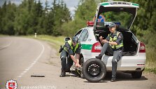 Akcijos &bdquo;Atsikratyk stereotipų&ldquo; fotosesijos kadras: kol kolega keičia tarnybinio automobilio ratą, jo porininkė lakuojasi nagus