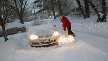 Vyras valo sniegą aplink savo automobilį.