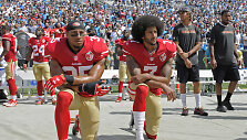 Ericas Reidas ir Colinas Kaepernickas neatsistojo per himną