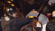 Policininkas protestuotojui trenkia lazda.