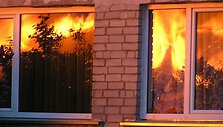Liepsnos atspindžiai gretimų namų languose.