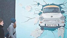 Turistai ir praeiviai tyrinėja meno kūrinius ant atrestauruotos 1,3 km ilgio sienos ruožo, vadinamo Rytų galerija &ndash; sieną pramu&scaron;a VDR simboliu tapęs automobilis &bdquo;Trabant&ldquo;.