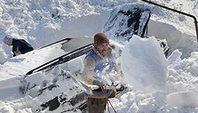 Vyrai atkasinėja apsnigtą automobilį.