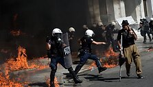 Graikijos policininkai bėga nuo protestuotojų mėtomų  padegamųjų bombų.