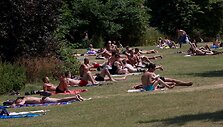 Pievoje žmonės mėgaujasi saulės voniomis. 