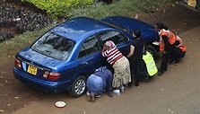 Pasigirdus &scaron;ūviams žmonės pasislėpė už automobilio.