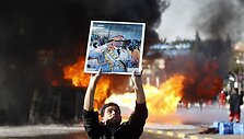 Protestuotojai laiko Muamaro Kadhafi portretą netoli degančio benzinvežio.