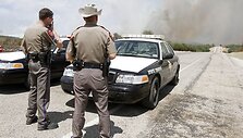 Policijos pareigūnai blokuoja kelią vedantį link nevaldomo gaisro.