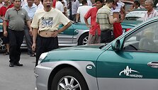 Taksi vairuotojas žiovauja &scaron;alia savo automobilio.
