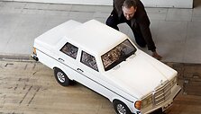 Darbuotojas pozuoja prie &bdquo;Mercedes-Benz&ldquo; automobilio formos karsto