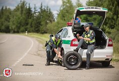 Akcijos &bdquo;Atsikratyk stereotipų&ldquo; fotosesijos kadras: kol kolega keičia tarnybinio automobilio ratą, jo porininkė lakuojasi nagus