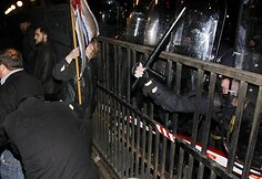 Policininkas bando nuvyti riaušininkus nuo tvoros.