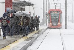 Žmonės, pasislėpę po skėčiais, laukia tramvajaus.